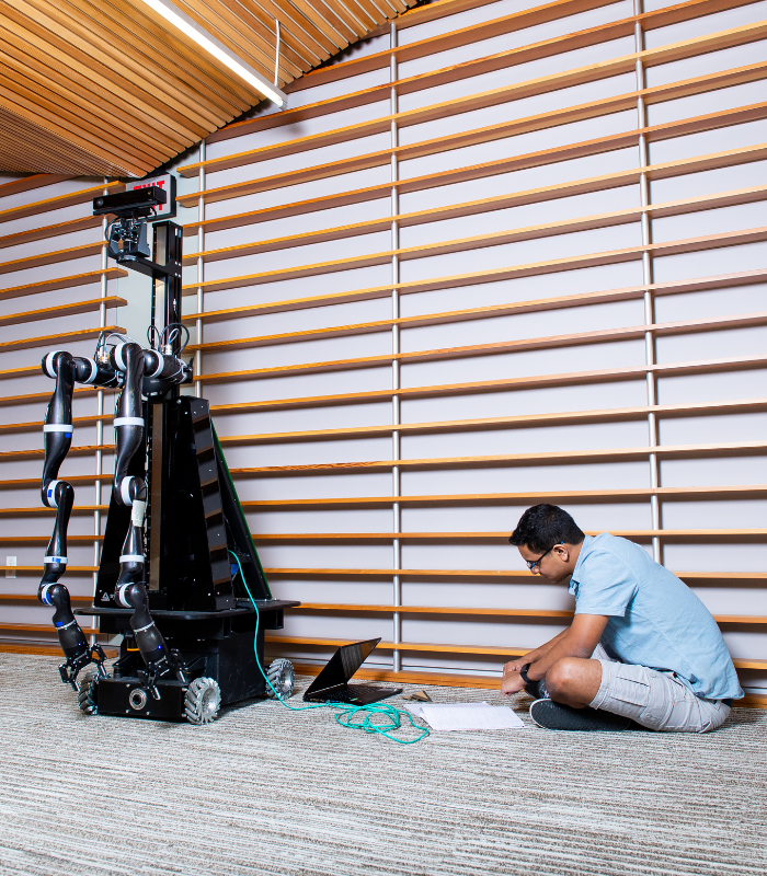 A robotics student sits on the ground of the GDC working on the technology of his robot.